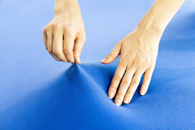 two hands stretching a navy blue fitted sheets showing how stretchy the cotton material