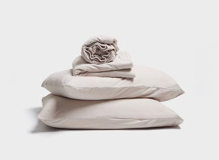 Beige  bed sheet set by It-Fits, featuring a stack of pillows with pillowcases, fitted sheet, and flat sheet designed for adjustable beds