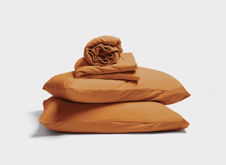 Jersey fitted sheet, top sheet and pillowcases in Ginger Brown by It-Fits arranged as a stack on plain background