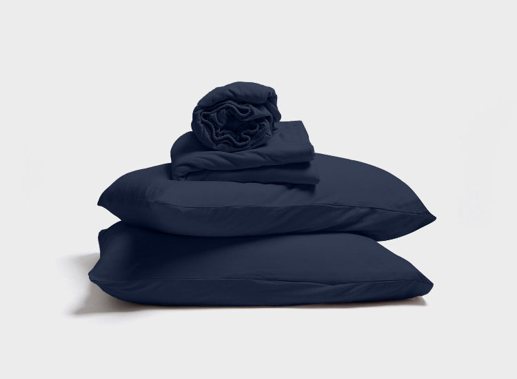 Navy blue sheet set by It-Fits, featuring a stack of pillow, pillowcase, fitted sheet, and flat sheet with deep pockets, ideal for adjustable beds on a simple background.