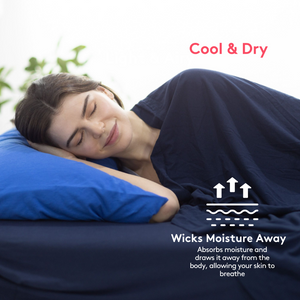 woman smiling covered flat sheet in navy blue while in bed with navy blue fitted sheet and royal blue pillow case, shows illustration of moisture away