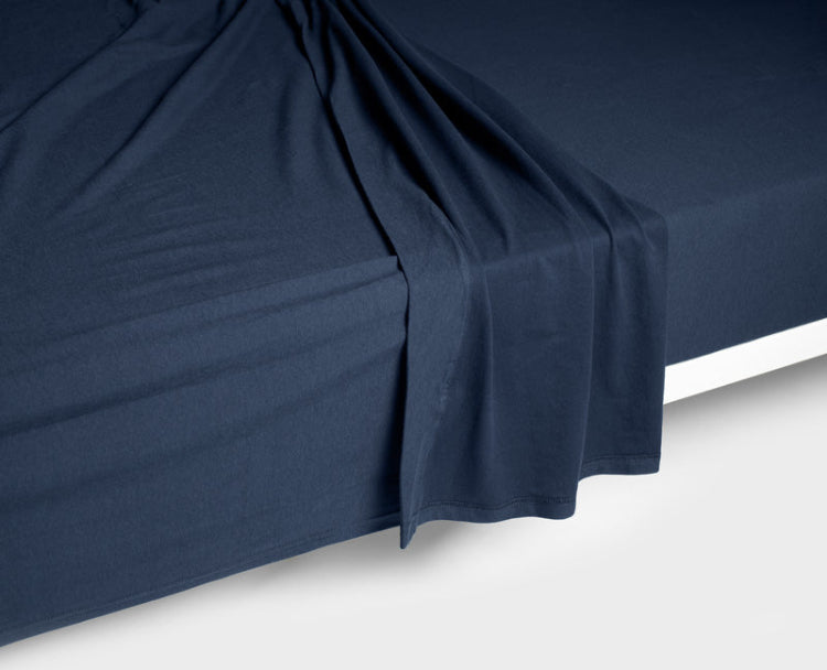 A navy blue flat sheet or top sheet loosely draped over a snugly navy blue fitted sheet on a bed, again a clean white floor.