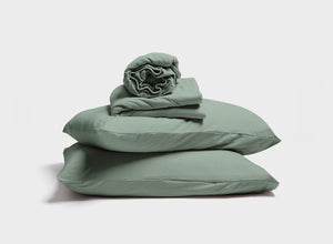 A stack of sage green pillow, pillowcase, fitted sheet, and flat sheet by It-Fits for adjustable beds, featuring deep pockets against a neutral background.