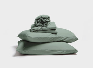 A stack of sage green pillow, pillowcase, fitted sheet, and flat sheet by It-Fits for adjustable beds, featuring deep pockets against a neutral background.