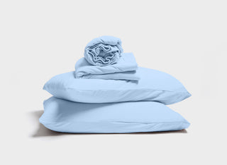 Sky blue sheet set by It-Fits, with a stack of pillow, pillowcase, fitted sheet, and flat sheet, featuring deep pockets, perfect for adjustable beds on a plain background.